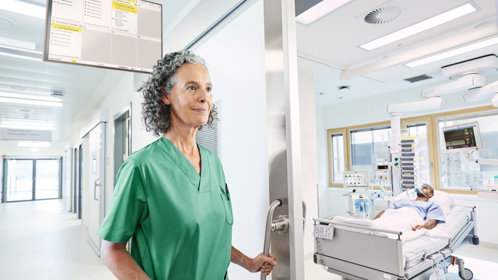 Nurse in the hospital corridor, equipped with silent ICU - in the room lies a patient in the intensive care unit